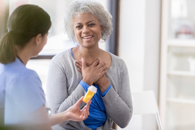 middle-aged-woman-expressing-gratitude-with-hands-on-heart-as-medical-professional-offers-prescription-medication-bottle