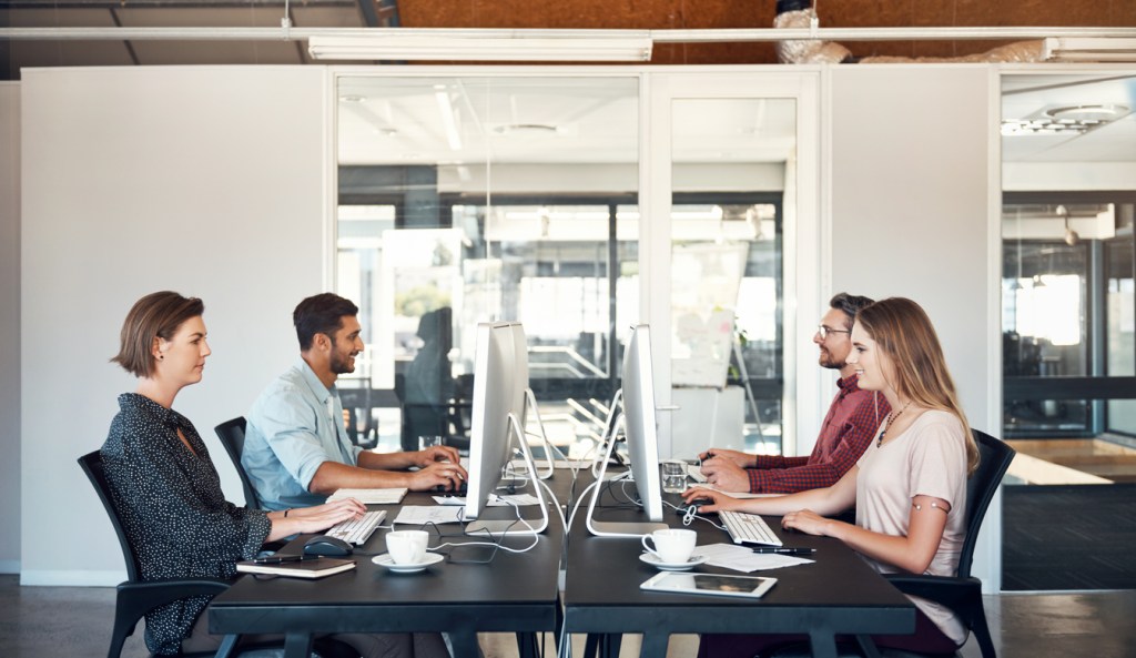 four-people-working-at-block-of-shared-desks-in-office-with-computers-and-keyboards