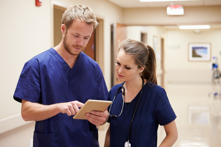 man and woman in scrubs looking at tablet while standing in hallway